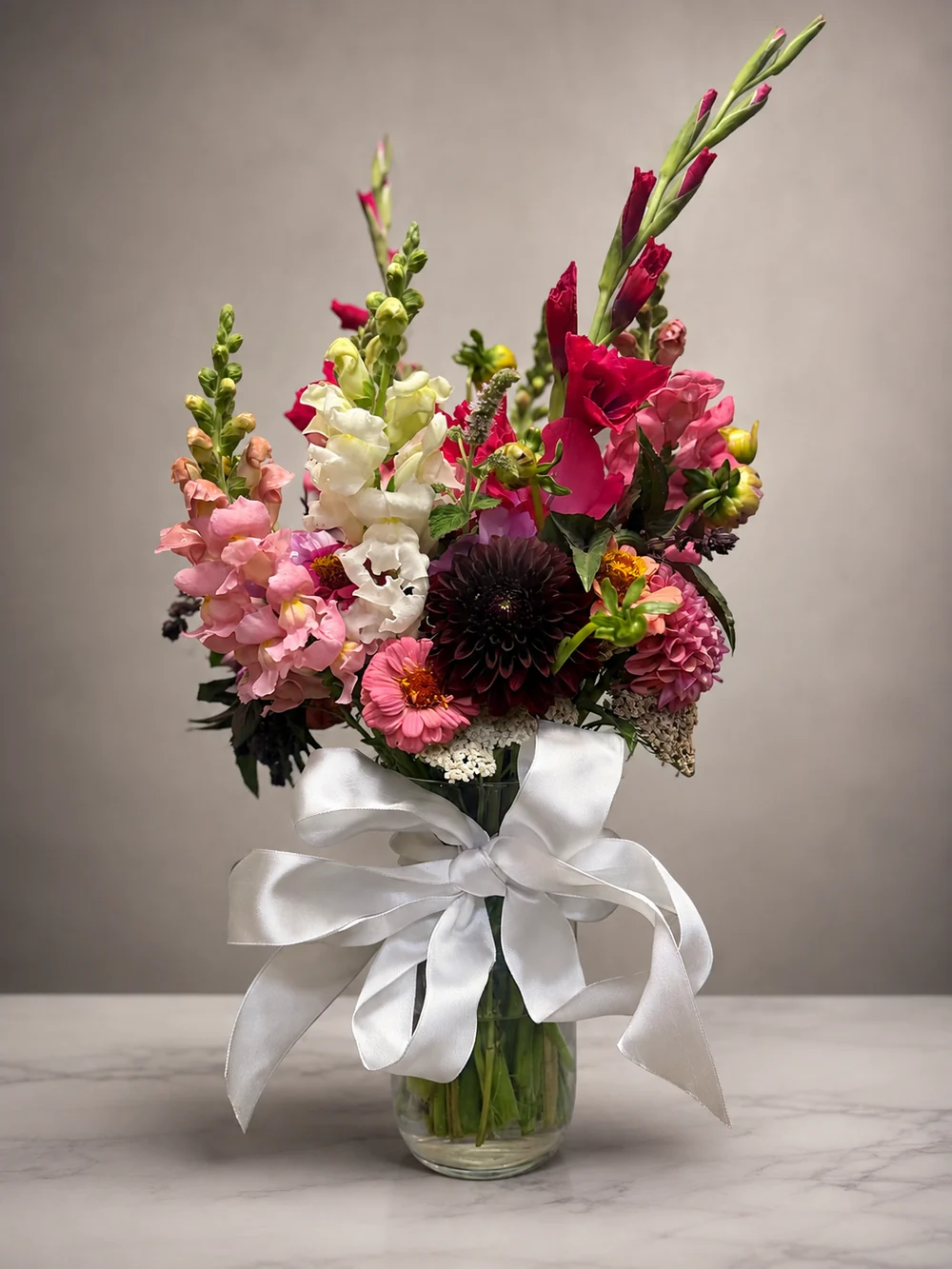 Colorful mixed flower arrangement in a glass vase tied with a white satin bow